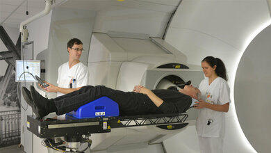Zwei_MTRA_lagern_am_Behandlungsplatz_einen_Patienten_zur_Bestrahlung_Foto_Uniklinikum_Dresden.jpg Zwei MTRA lagern am Behandlungsplatz der Universitäts ProtonenTherapie einen Patienten