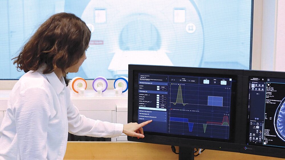 MRT-Framework.jpg Ärztin im Vorraum des MRT, im Hintergrund zu sehen, und zeigt etwas an einem Bildschirm