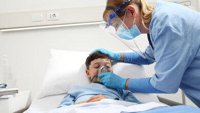 Kind_mit_COVID_19_in_Klinik.jpg Kind mit COVID-19 bekommt in der Klinik Sauerstoff von einer Pflegerin.