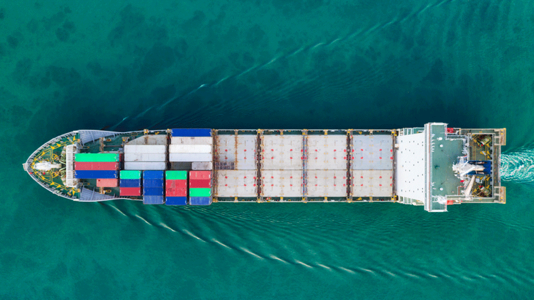 2026-03-03-Foto-Pressemeldung-_c_BPI_Shutterstock_Studio-concept_1175688757.gif Dieses Bild zeigt eine Luftaufnahme eines Frachtschiffs, das durch klares, blaues Wasser fährt. Das Schiff transportiert mehrere bunte Container, die vermutlich für den Gütertransport verwendet werden.