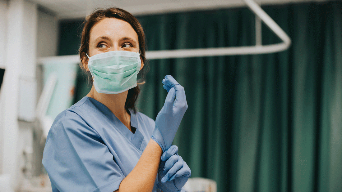 AdobeStock_245289970.gif Das Bild zeigt eine medizinische Fachkraft in einer klinischen Umgebung, die Schutzkleidung und Handschuhe trägt und sich auf eine Untersuchung oder einen Eingriff vorbereitet.