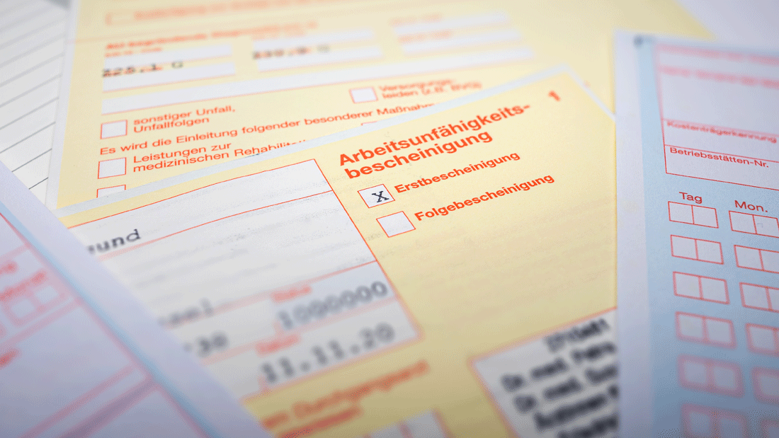 AdobeStock_427265584.gif Mehrere gelbe Formulare zur Arbeitsunfähigkeitsbescheinigung liegen übereinander. Markiert ist eine Erstbescheinigung.