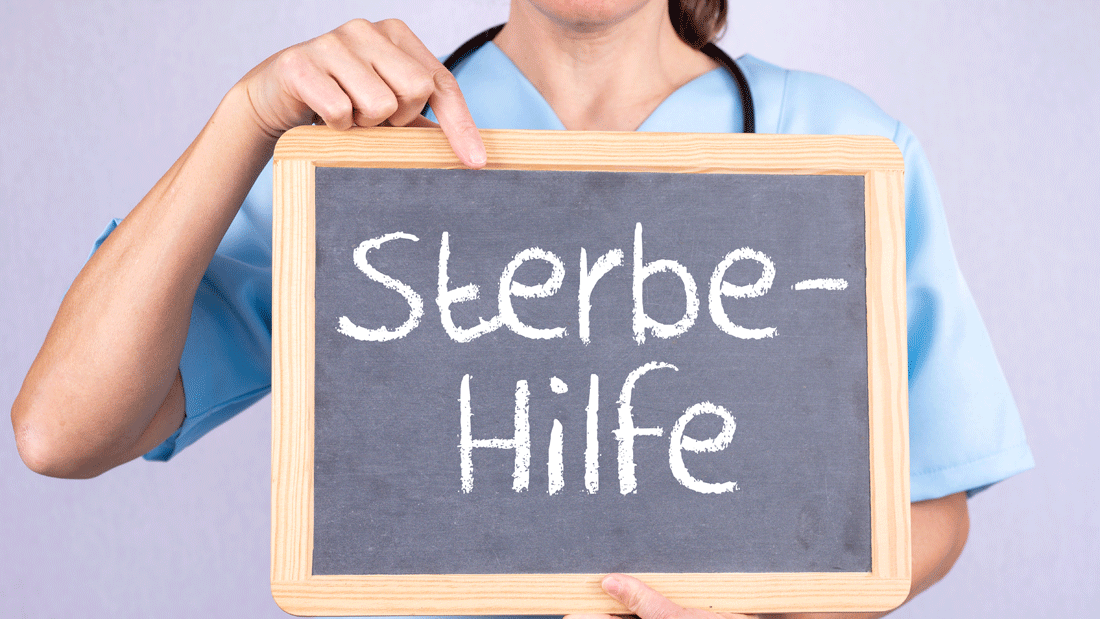 AdobeStock_494177376.gif Eine Person in medizinischer Kleidung hält eine Tafel mit der Aufschrift „Sterbe-Hilfe“.