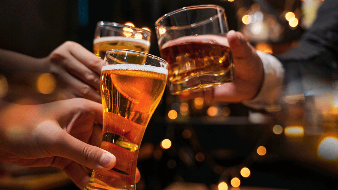 AdobeStock_513239634.gif Mehrere Hände stoßen in Bar-Atmosphäre mit Bier- und Whiskygläsern an.