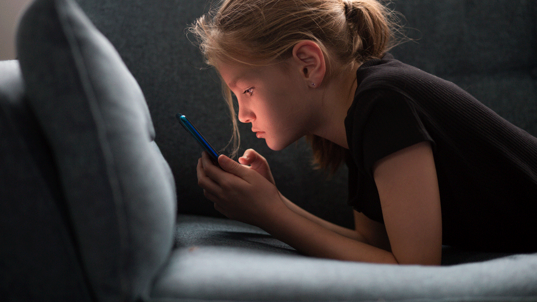 AdobeStock_577024134.gif Das Bild zeigt ein Mädchen, das auf einem Sofa liegt und ein Smartphone benutzt.